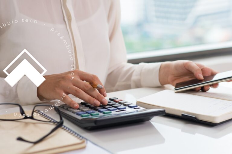 Advogada sentada à mesa utilizando uma calculadora e celular para fazer o contato com a pessoa certa.